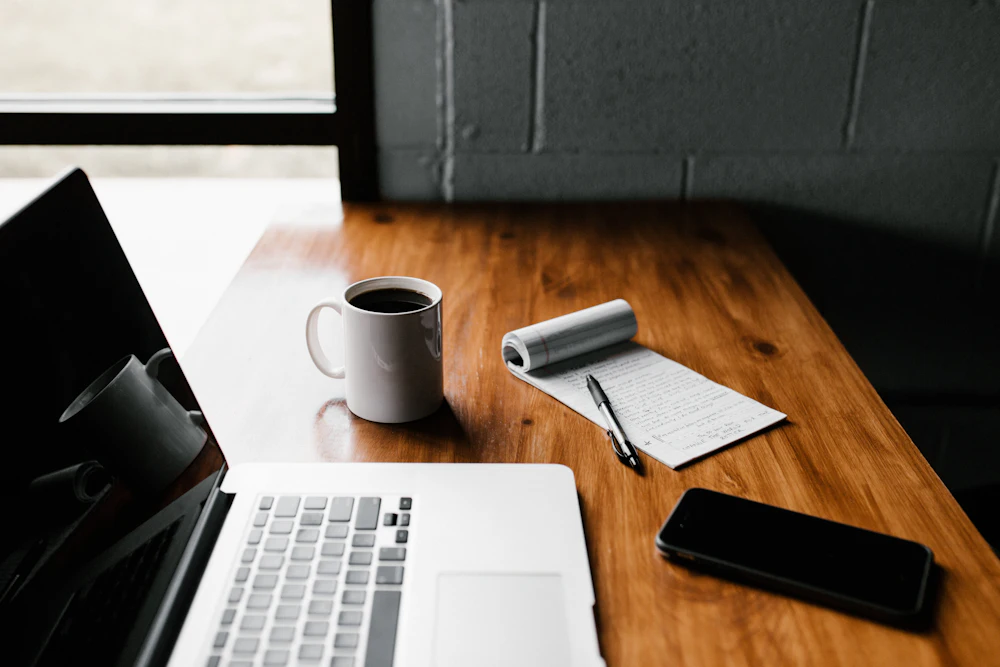 A warm desk with a laptop, notebook and coffee